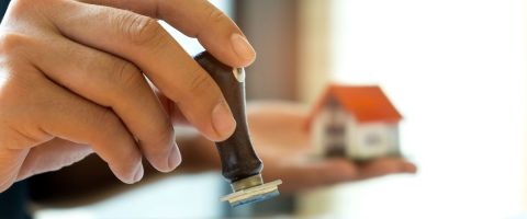 יד אוחזת בחותמת על רקע מודל של בית