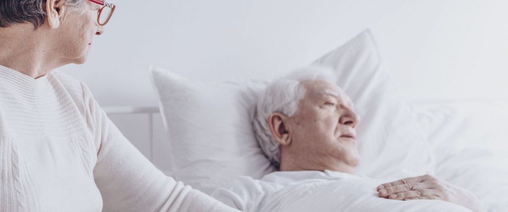 אישה אוחזת בידו של גבר תשוש נפש במיטתו