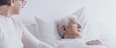 אישה אוחזת בידו של גבר תשוש נפש במיטתו